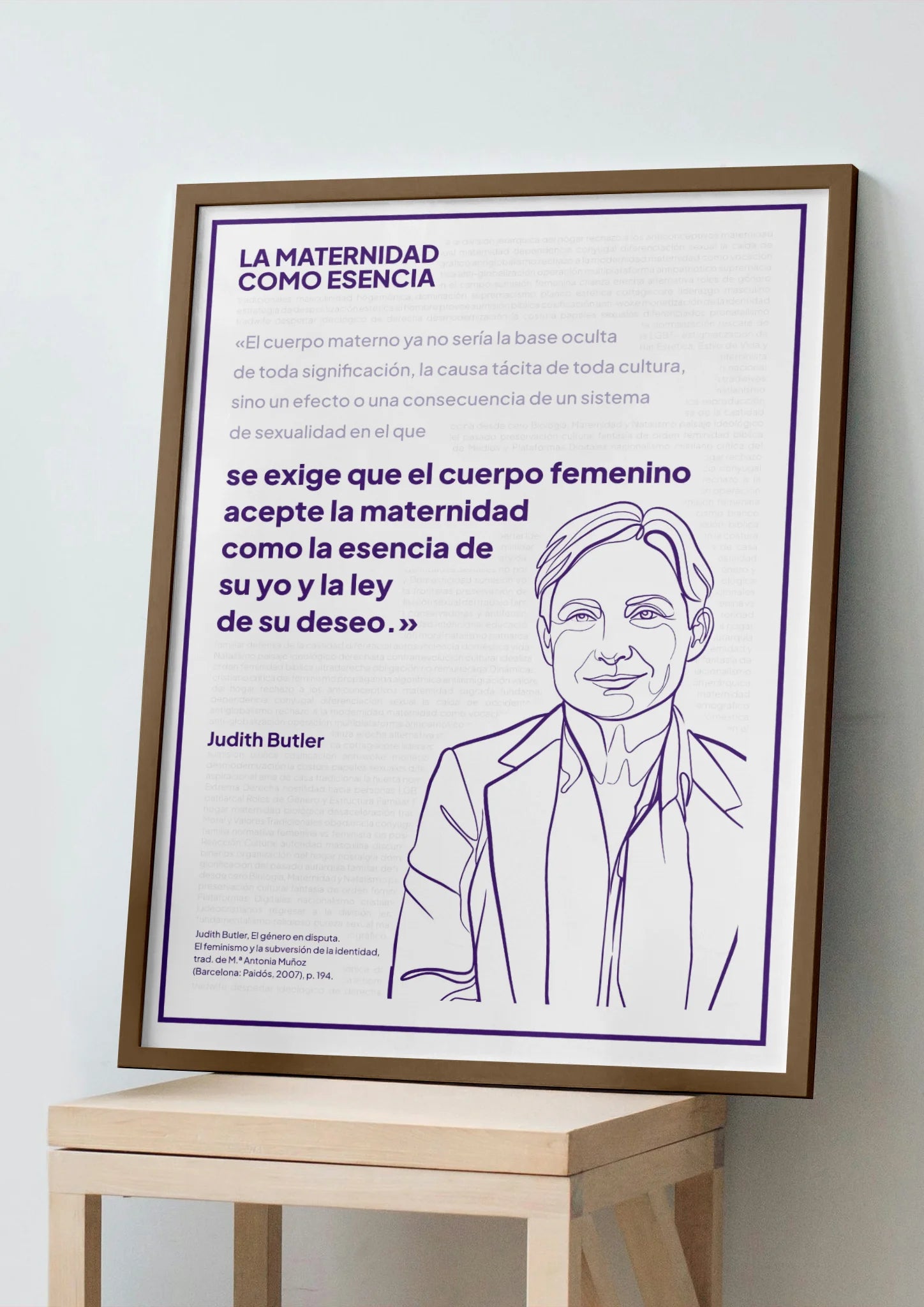 Afiche violeta de Judith Butler enmarcado, apoyado sobre un banco de madera clara.