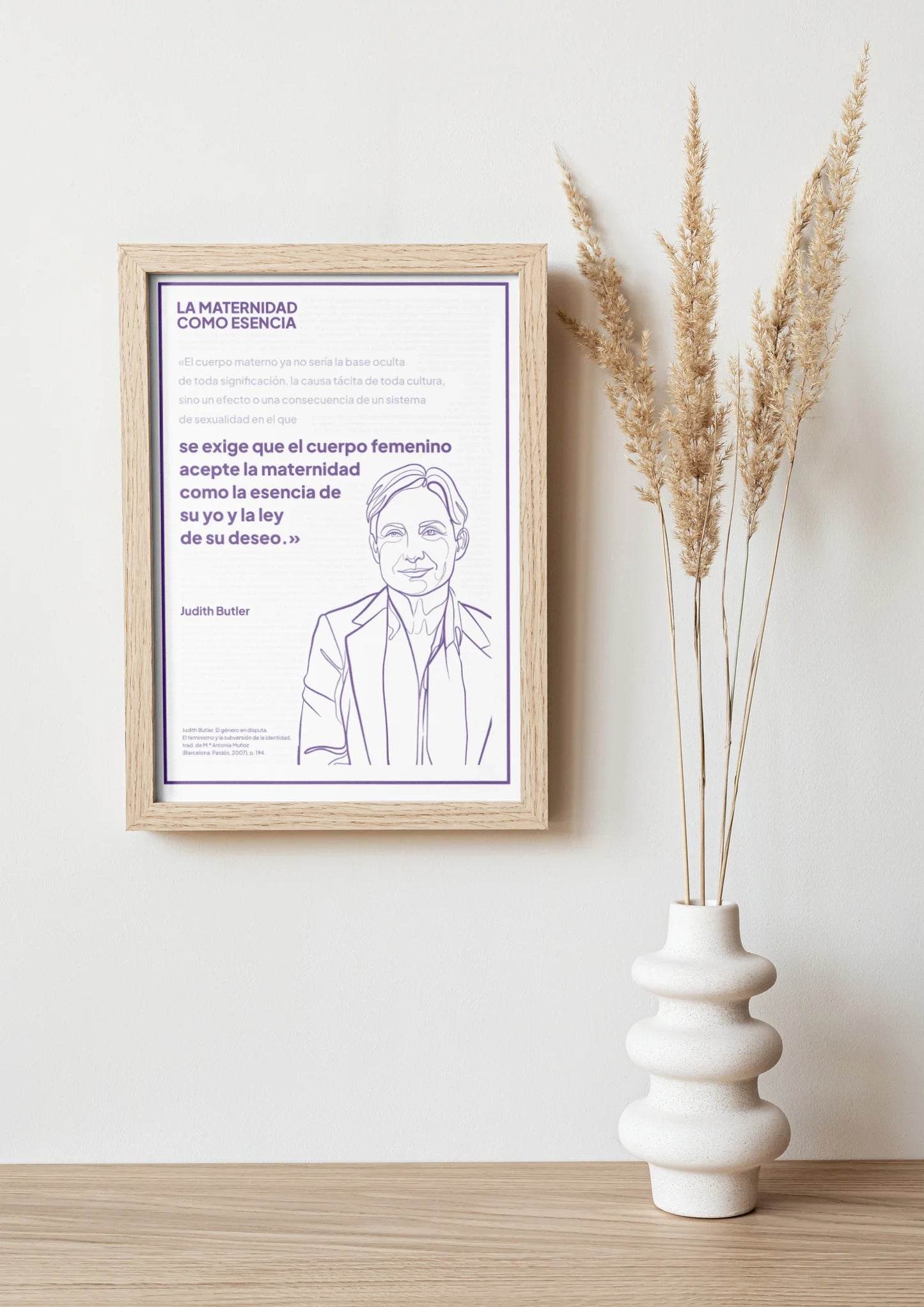 Afiche violeta de Judith Butler enmarcado sobre una repisa con jarrón y ramas secas.
