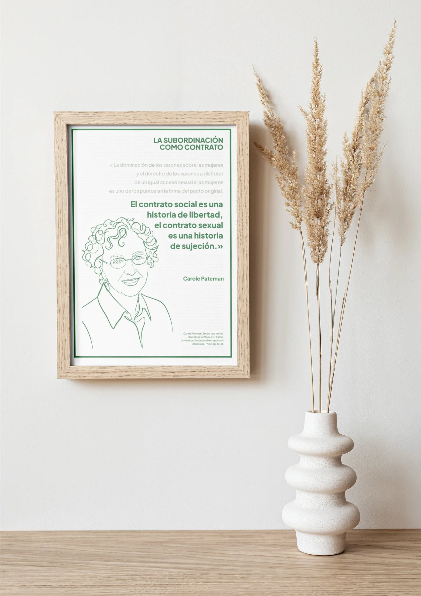 Afiche verde de Carole Pateman enmarcado sobre una repisa con jarrón y ramas secas.
