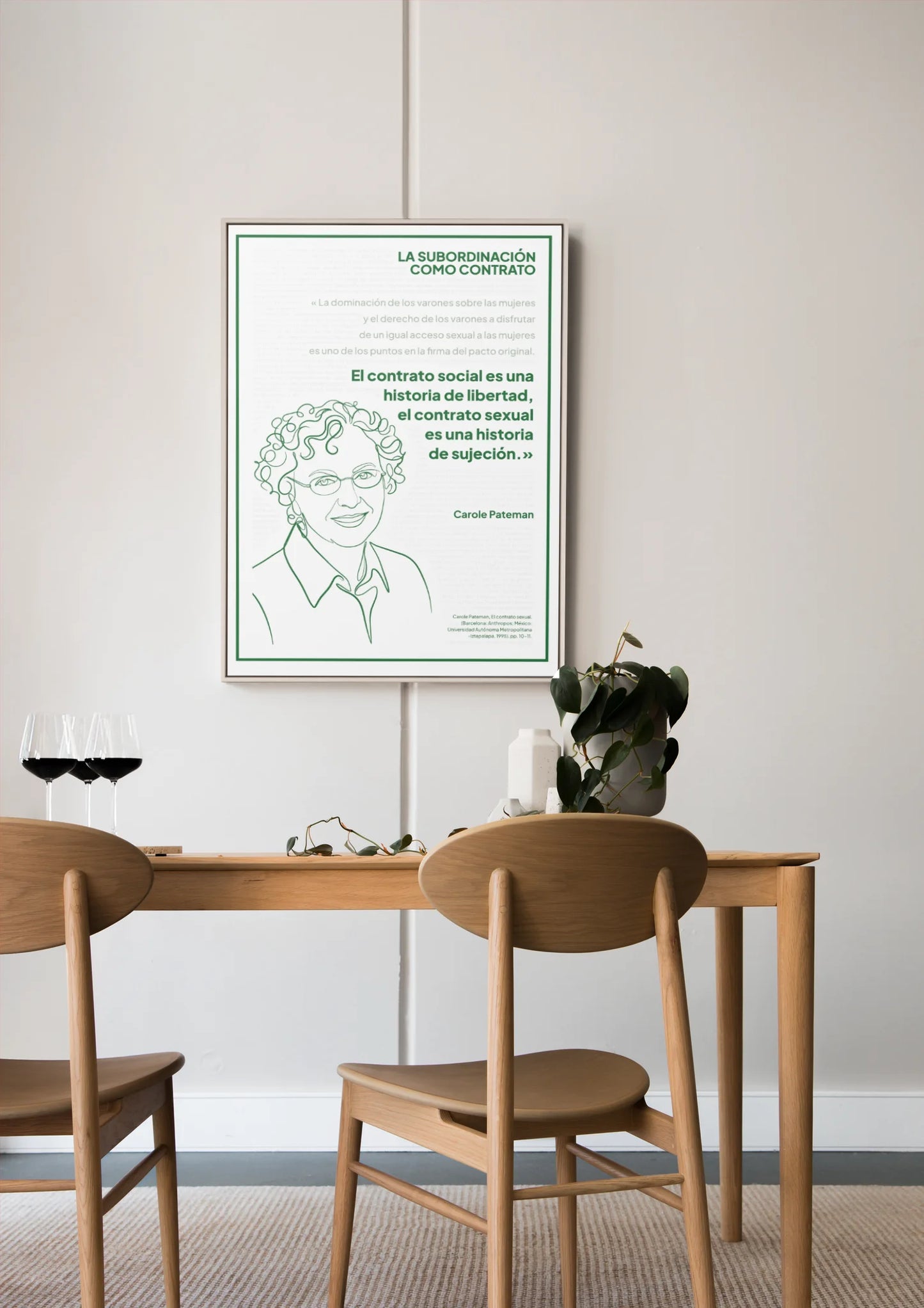 Afiche verde de Carole Pateman enmarcado sobre una mesa de comedor de madera.