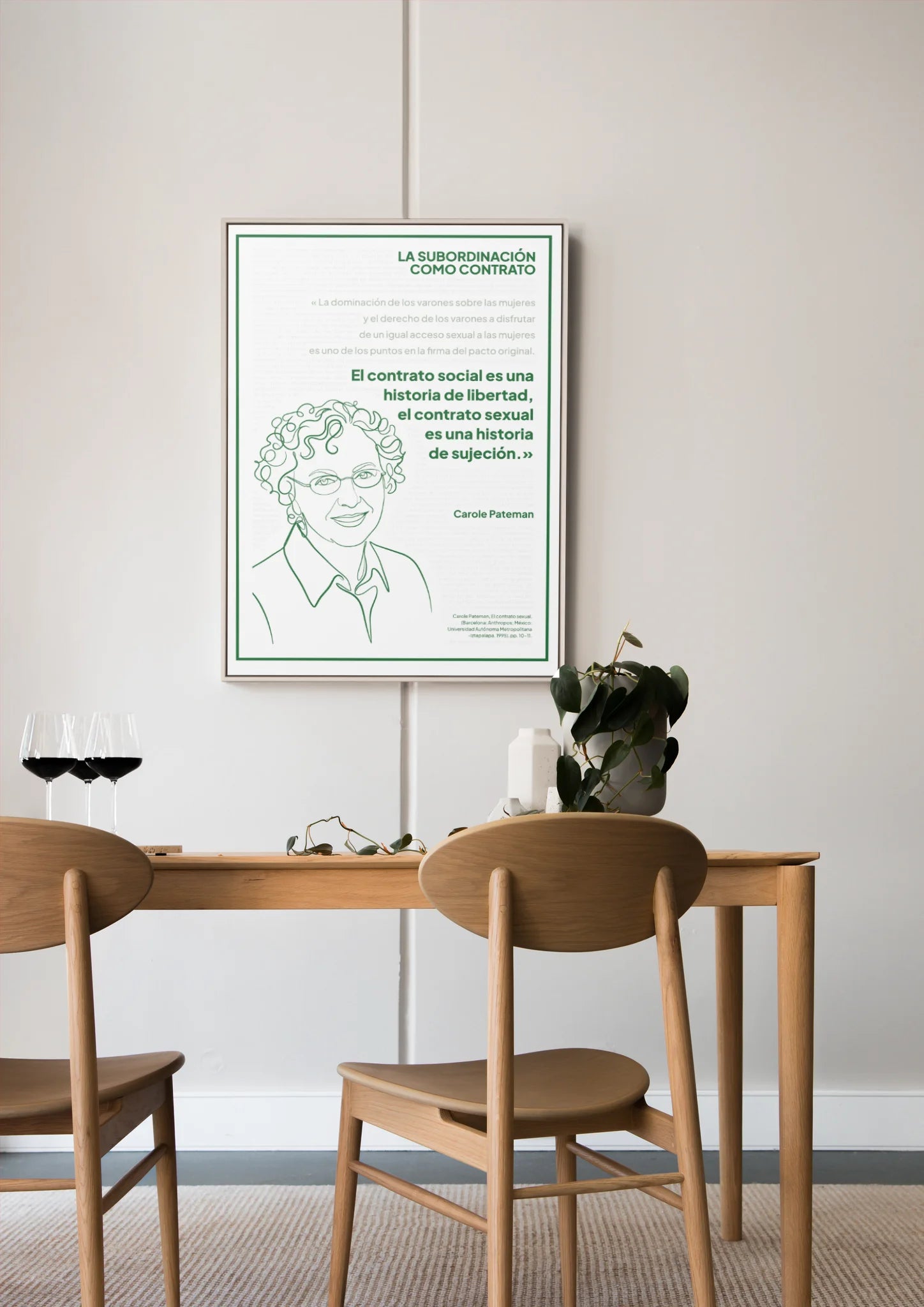 Afiche verde de Carole Pateman enmarcado sobre una mesa de comedor de madera.